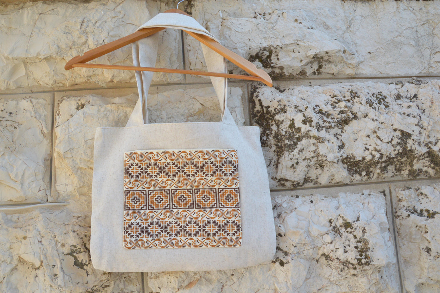 Tote bag with a patterned design hanging on a wooden hanger against a stone wall.