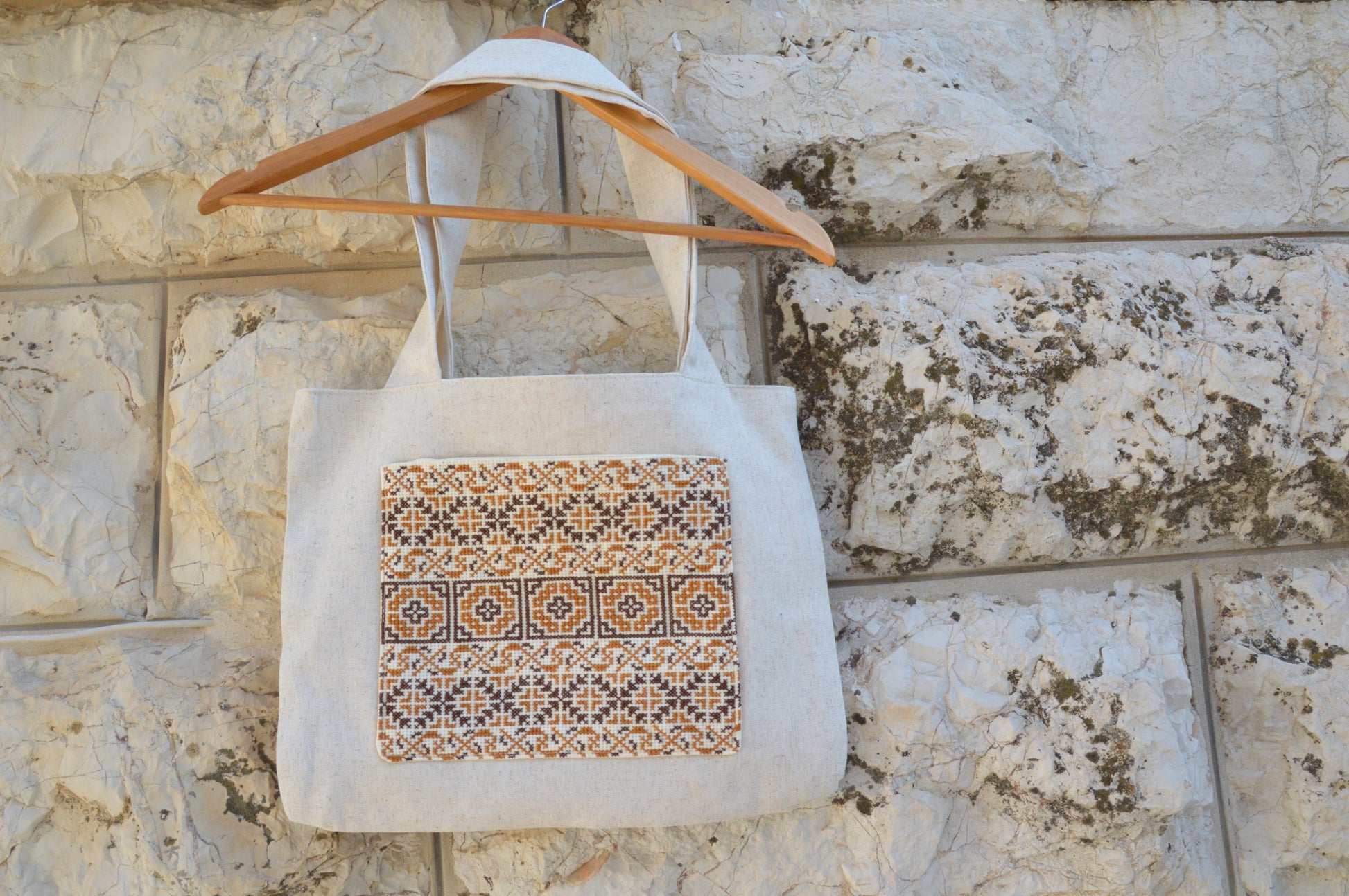Tote bag with a patterned design hanging on a wooden hanger against a stone wall.