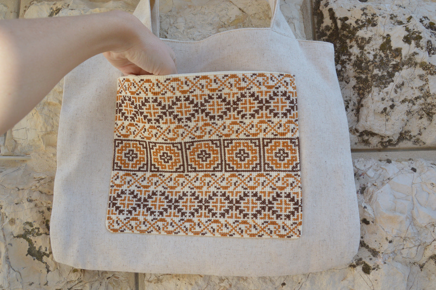 Tote bag with a geometric pattern held by a hand against a stone wall background
