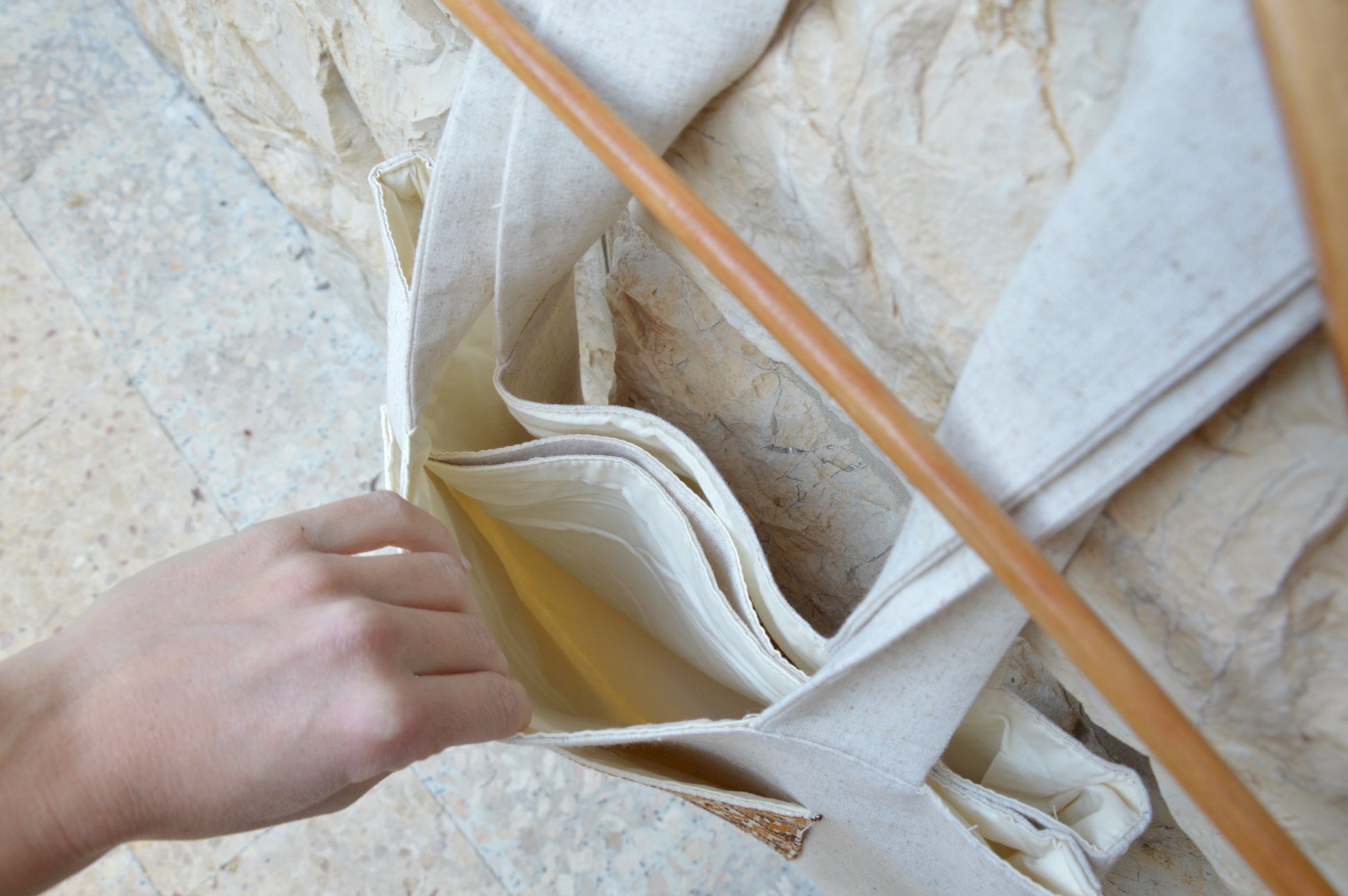 Person holding a beige fabric bag with a wooden stick on a textured surface