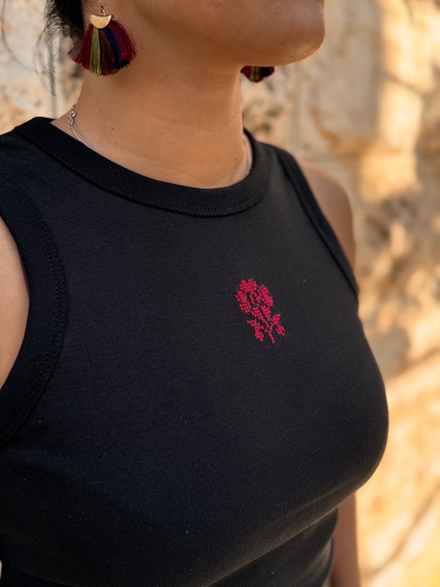 Person wearing a black sleeveless top with a red floral embroidery detail.