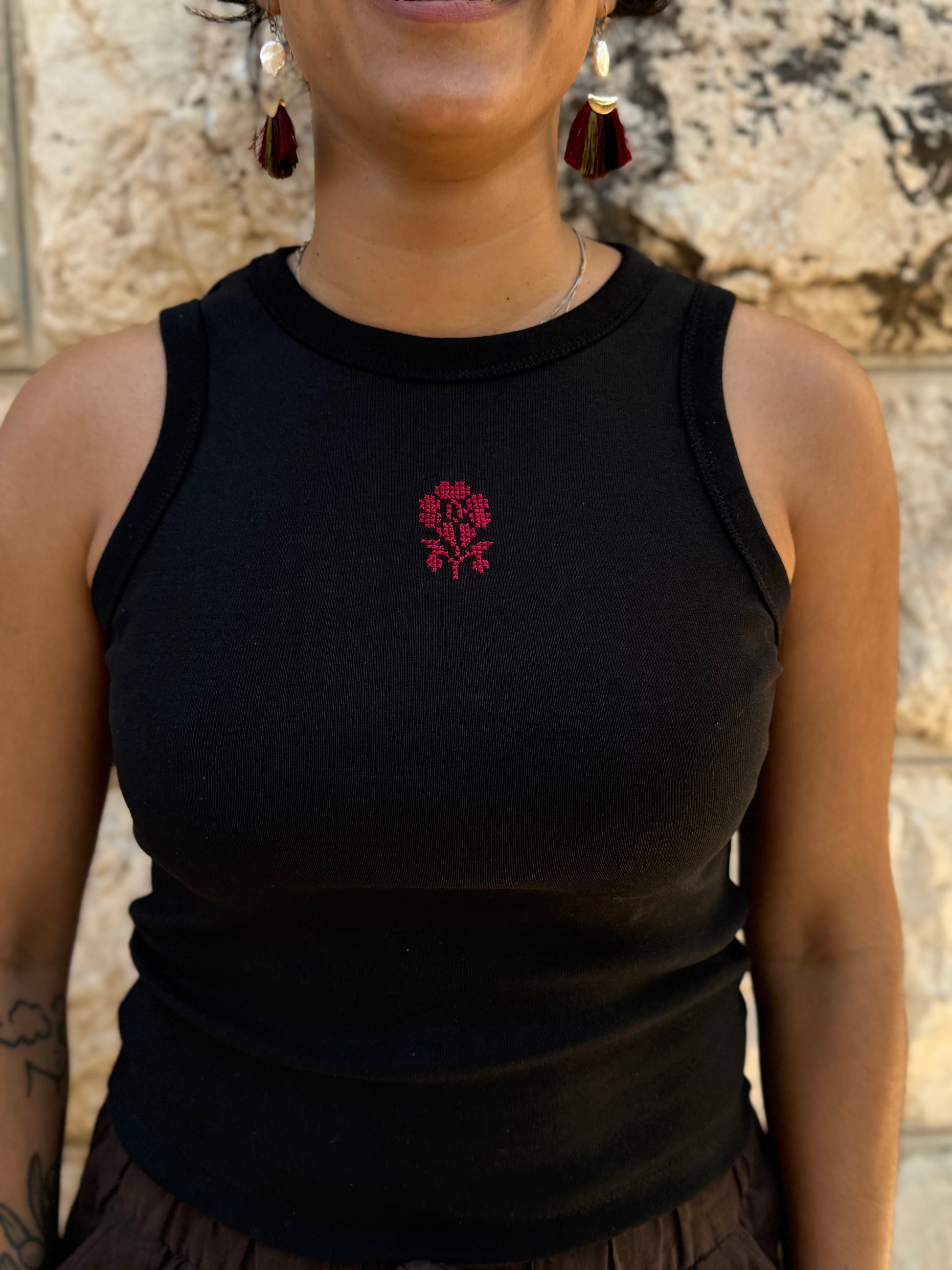 Person wearing a black tank top with a red floral design against a stone wall background