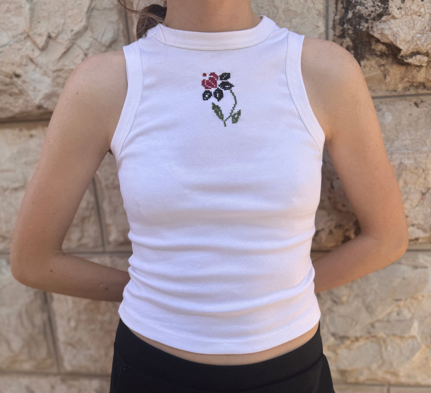 Person wearing a white tank top with a floral design against a stone wall background