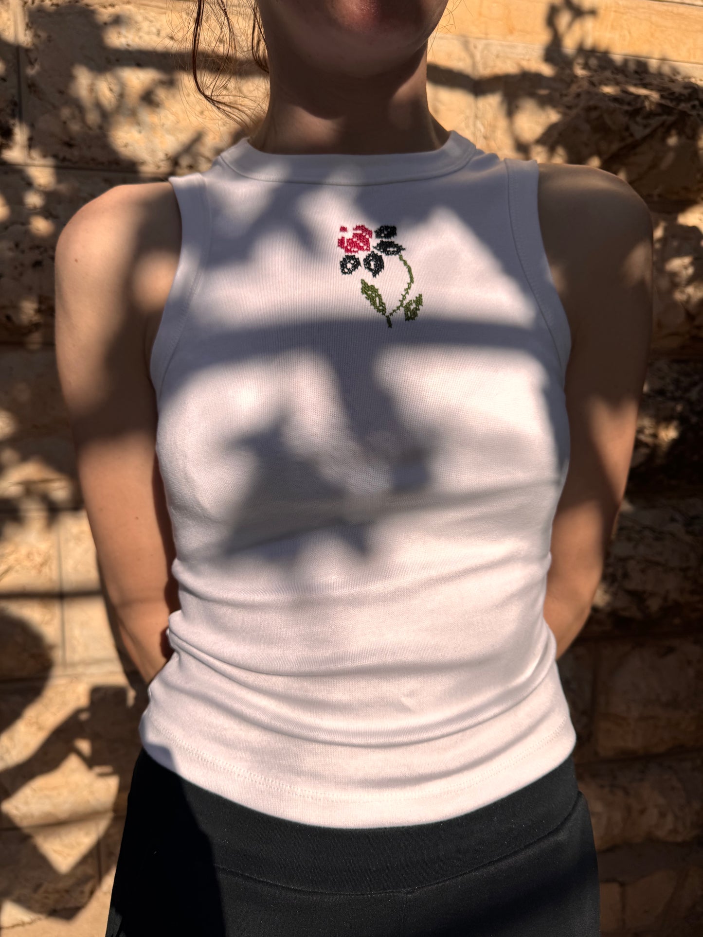Person wearing a white tank top with a floral design on a sandy background