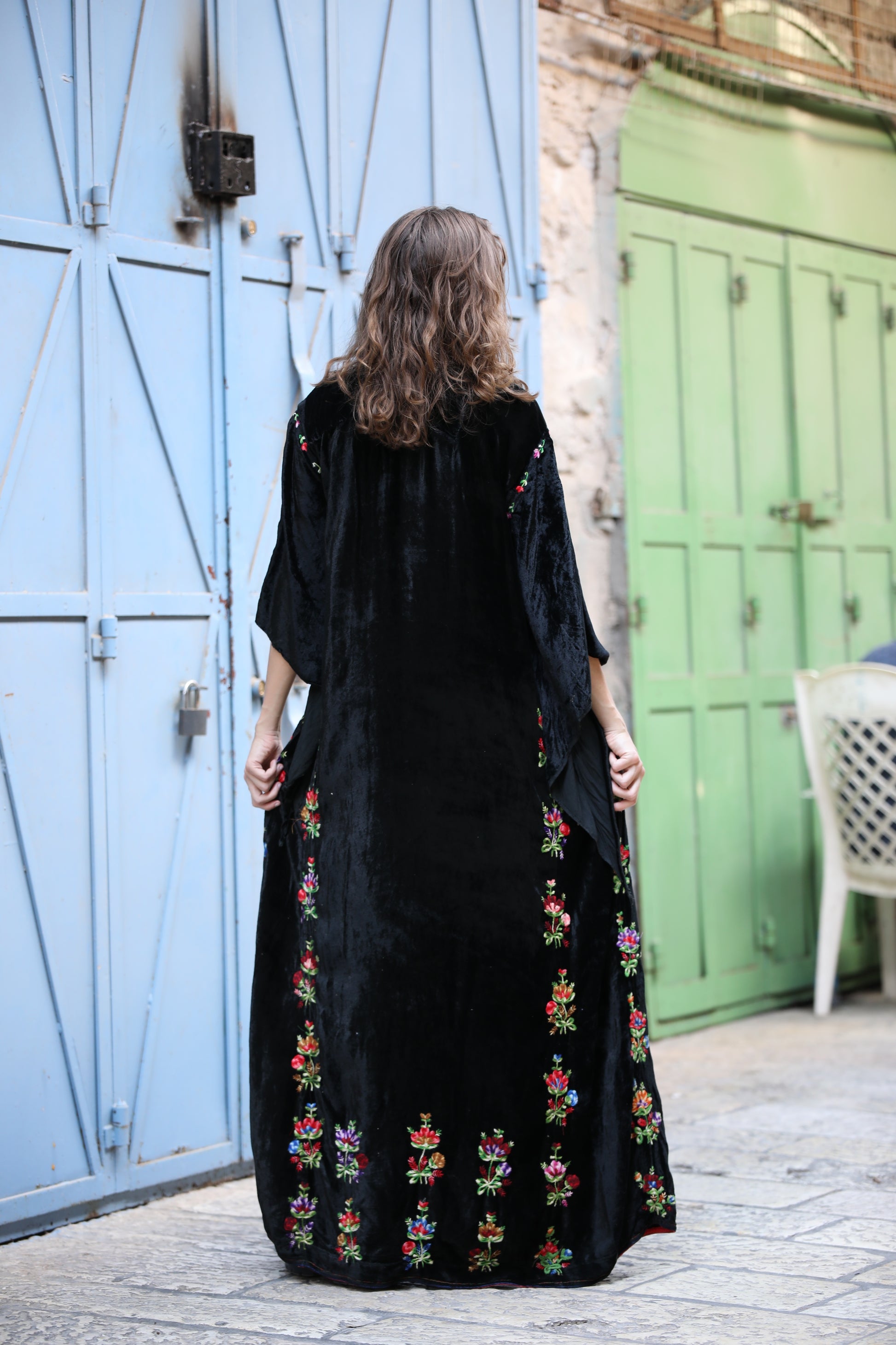 Woman wearing a black dress with colorful embroidery standing in front of a blue and green door.